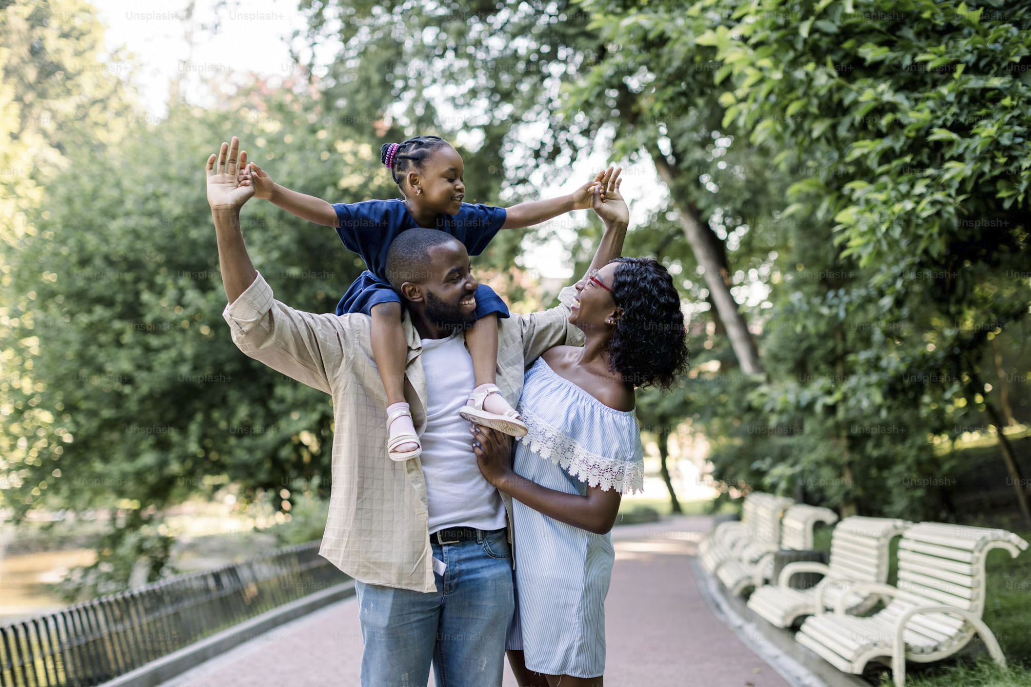 Black family laughing in park, daughter on dad's shoulders